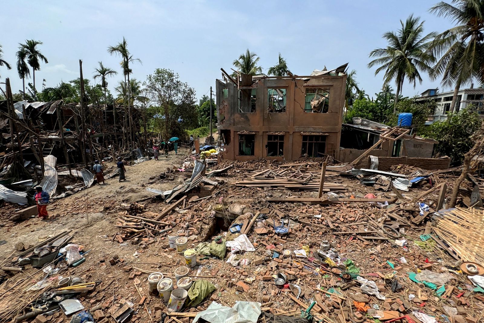 People walk past buildings destroyed by a regime airstrike in Rakhine State’s Kyauktaw town on May 15, 2025. (AFP)