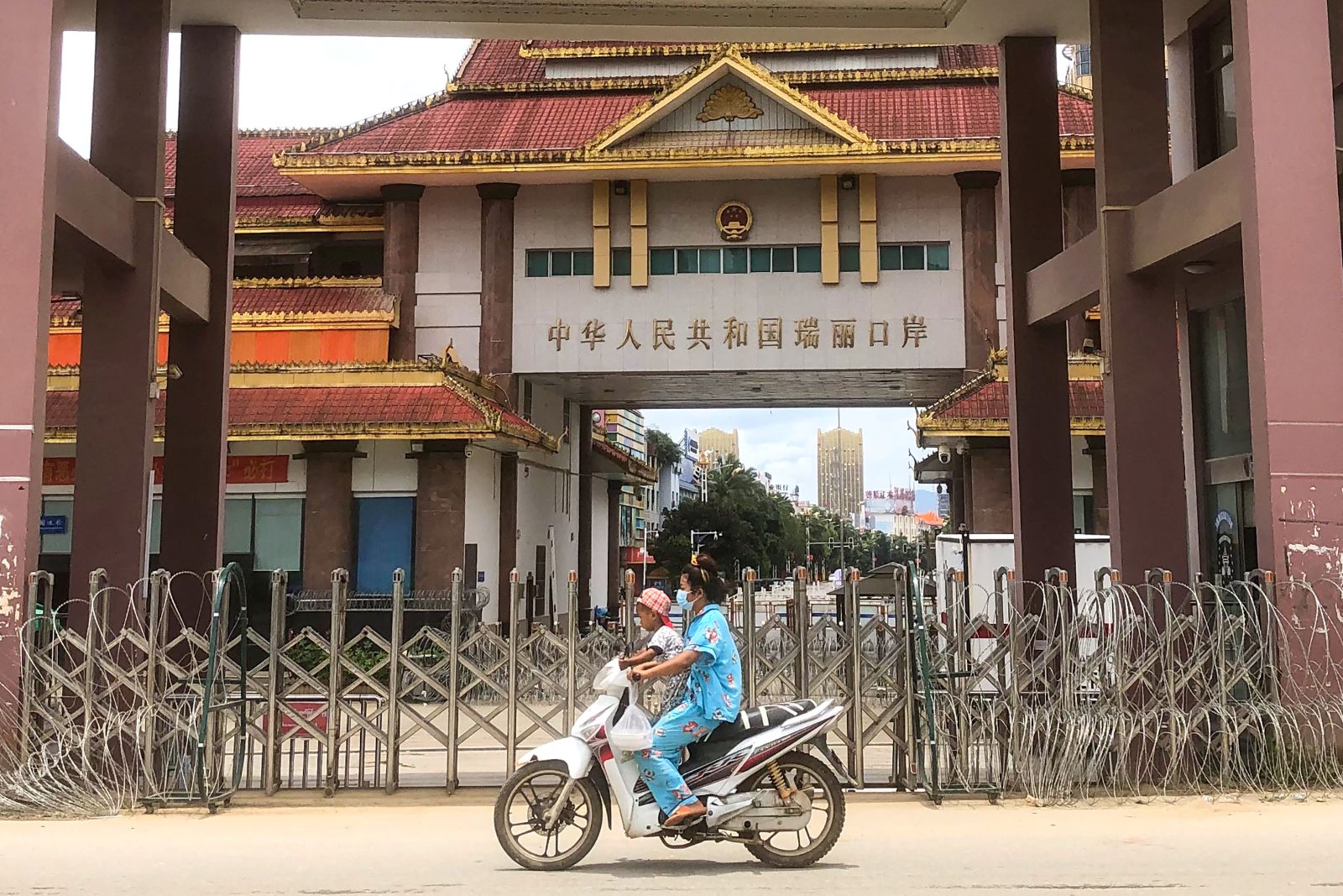 A woman rides a scooter with a child past the China-Myanmar border gate in northern Shan State's Muse town on July 5, 2021. (AFP)