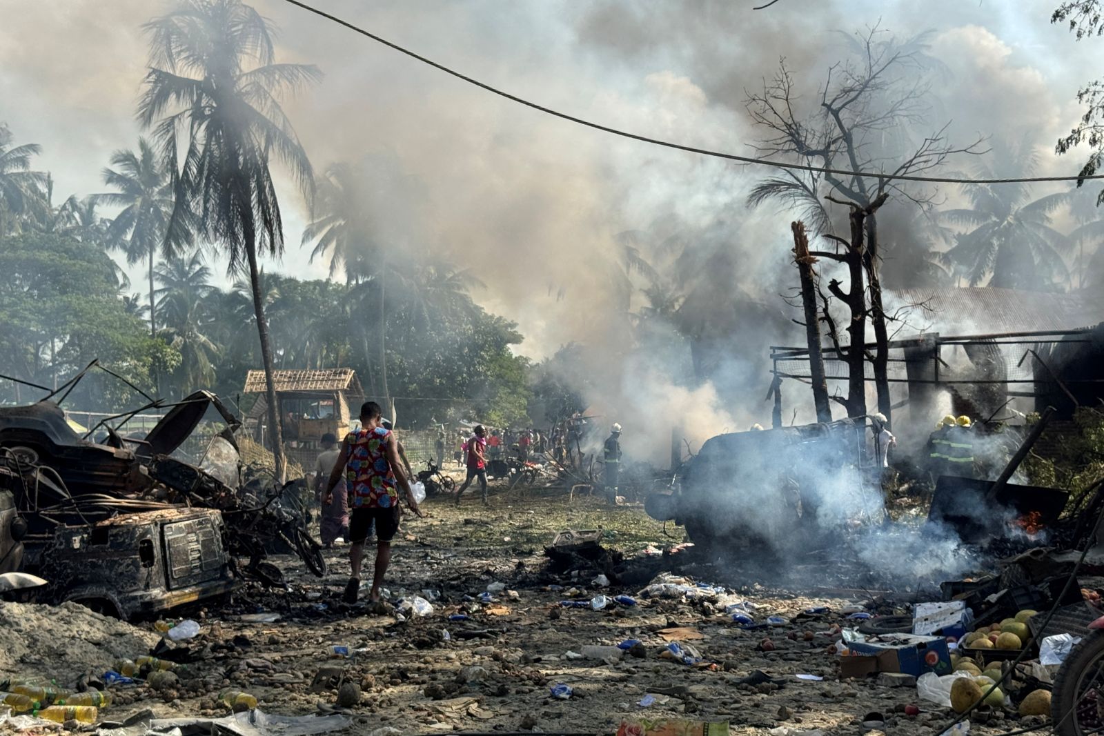People walk through smoke and smouldering debris following a regime airstrike on a market and adjacent bridge in Rakhine State’s Kyauktaw town on September 28. (AFP)